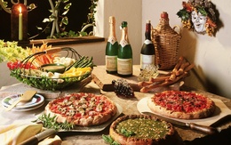 3d обои Итальянская кухня. Пышно накрыт стол-пиццы с разными начинками, овощи, красиво нарезанные, там можно различить спаржу, виднеются ещё грибы, посредине этого блюда соус, стол также украшают и изысканные вина, горит свеча и над столом висит маска Бахуса