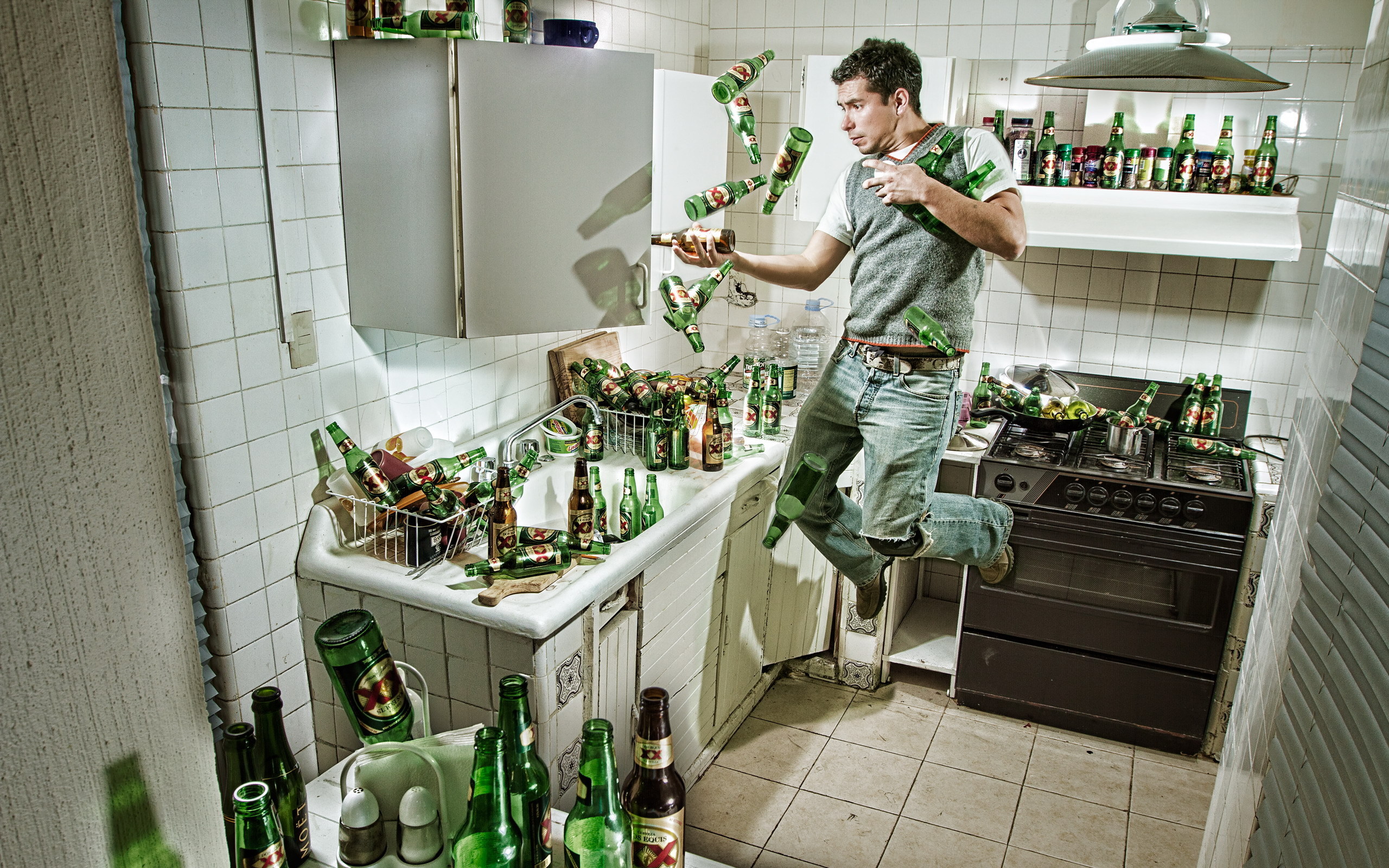 3d обои Мужчина на кухне в вязаной безрукавке пытается поймать падающие пустые пивные бутылки, которыми заставлена вся кухня (dos equis)  реклама # 76209